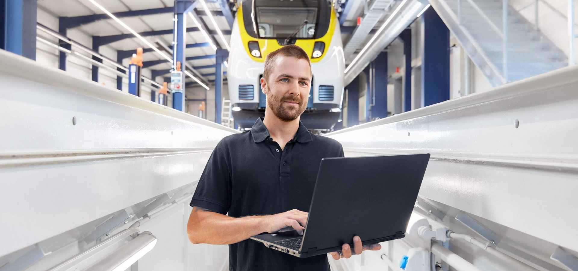 Ein Mann mit Laptop steht vor einem Zug in der Wartungshalle