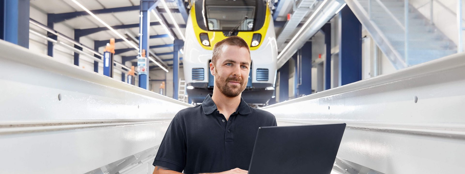 Ein Mann mit Laptop steht vor einem Zug in der Wartungshalle